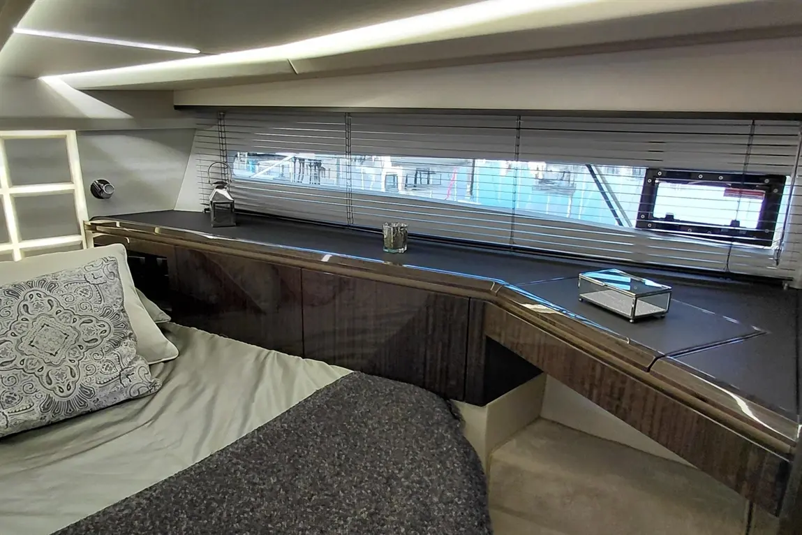 Luxurious bedroom with a neatly made bed, decorative pillow, and a stylish desk by a window with blinds, overlooking a marina.